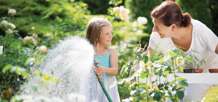 Grandchild watering garden with hose.