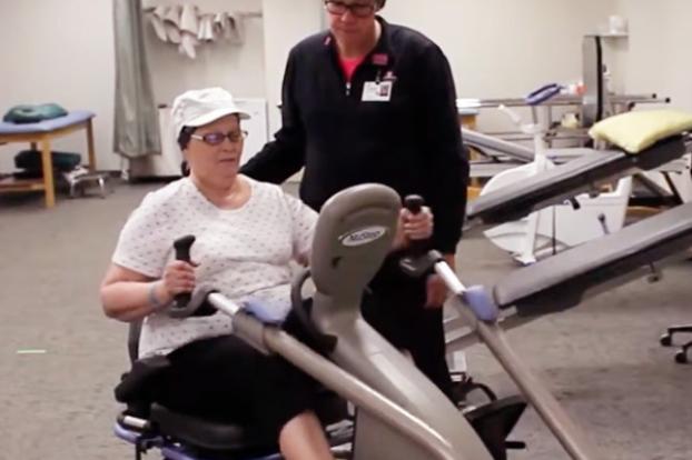 Cancer patient on stationary bike with therapist supervising.