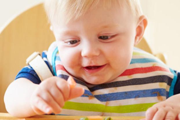 Toddler grasping food on highchair tray