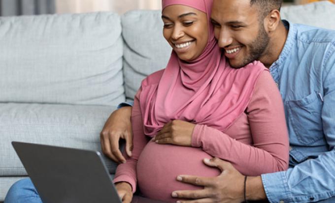 Pregnant couple looks at laptop