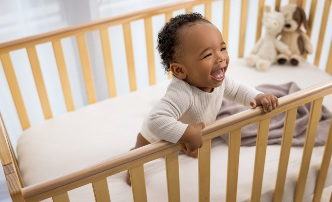 Baby boy smiles while leaning inside a crib