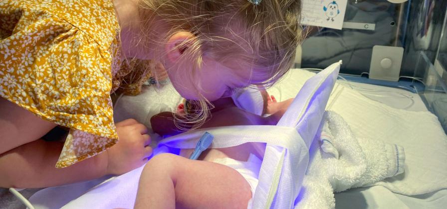 Sibling visits infant in NICU incubator.