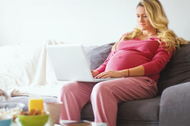Pregnant at home on couch with laptop.